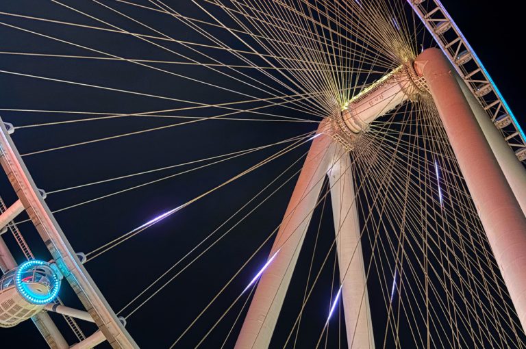 Diagonal view of Ain Dubai at night, showing illuminated spokes, steel cables and a cabin against a dark sky.