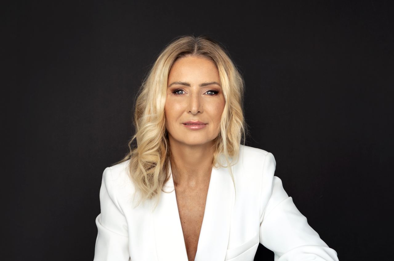 Portrait of Dr. Heike Lieb-Wilson in a white blazer against a dark background, looking directly at the camera.