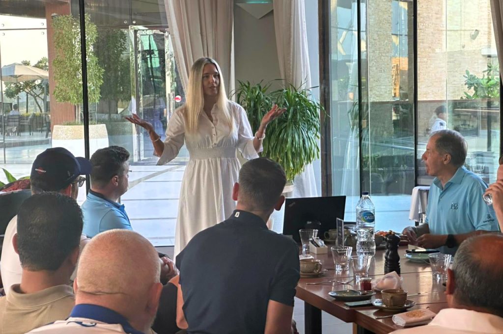 Anna Thiel in a white dress standing in front of seated participants, giving a talk to entrepreneurs in a Dubai restaurant setting.