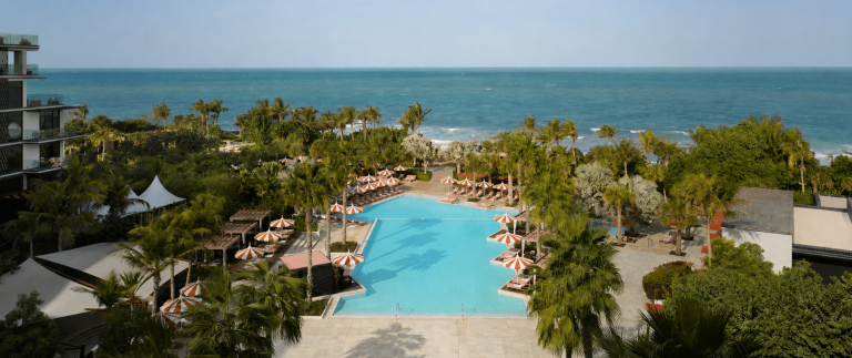 Luxury tropical wellness resort with turquoise pool, palm trees, ocean view, and peaceful outdoor relaxation areas.